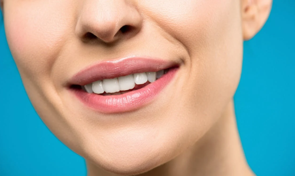 A close-up of a smiling woman with white teeth and pink lipstick